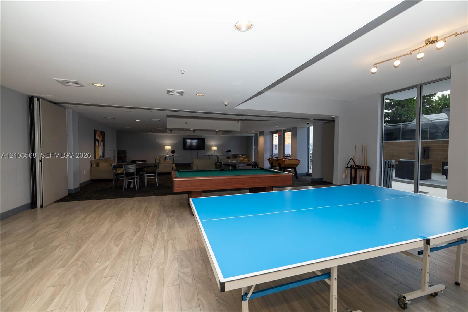 Open-concept recreational space featuring wood-finish flooring, recessed lighting, multi-directional track lighting, and floor-to-ceiling glass sliding doors