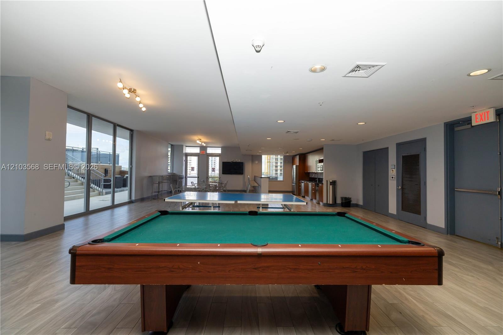 Spacious recreation area featuring wood-finish flooring, recessed lighting, floor-to-ceiling windows, and a built-in kitchenette