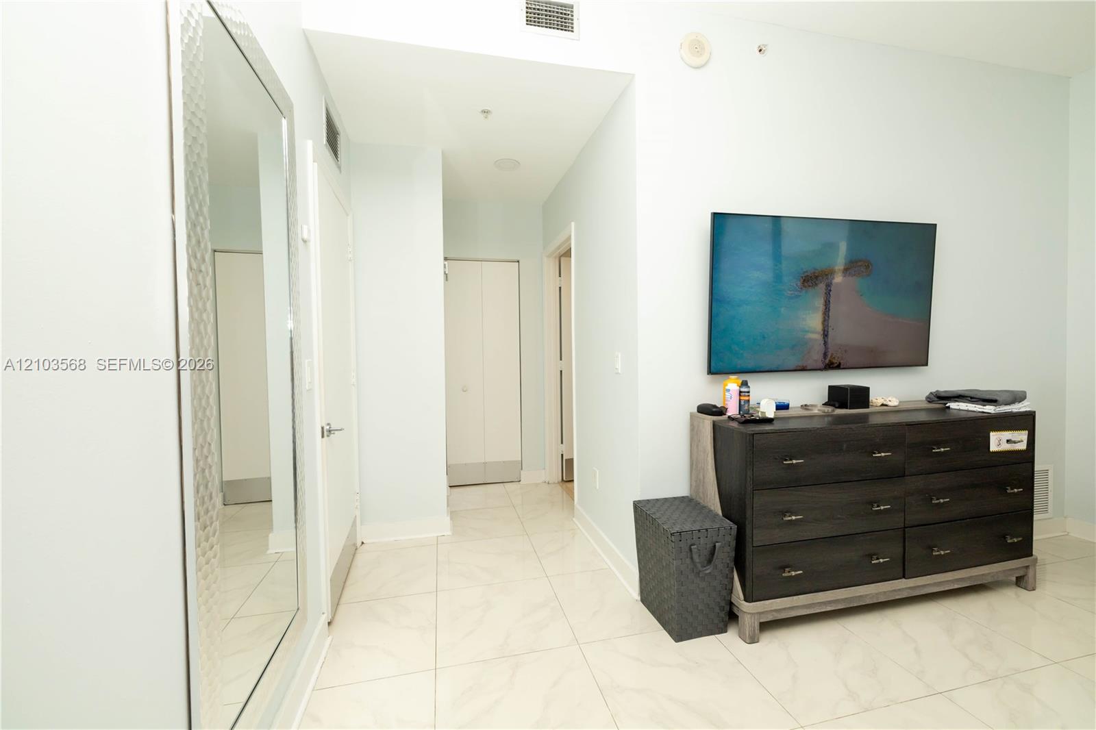Large-format floor tile, full-length wall mirror with textured frame, and white solid-core doors