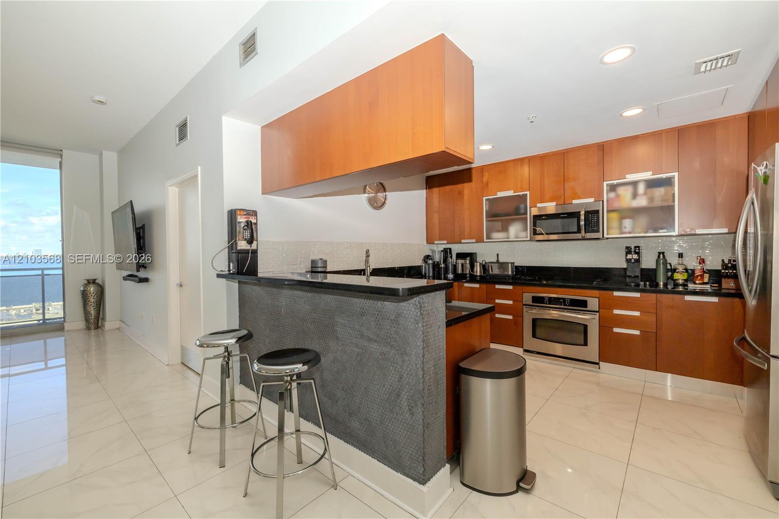 Kitchen featuring wood cabinetry, stone countertops, stainless steel appliances, and a tiled breakfast bar