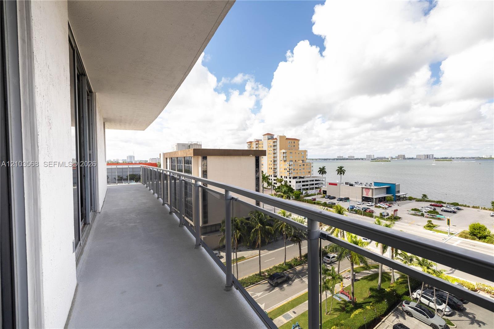 Covered balcony featuring concrete flooring and a metal railing with glass panels, showcasing a water backdrop