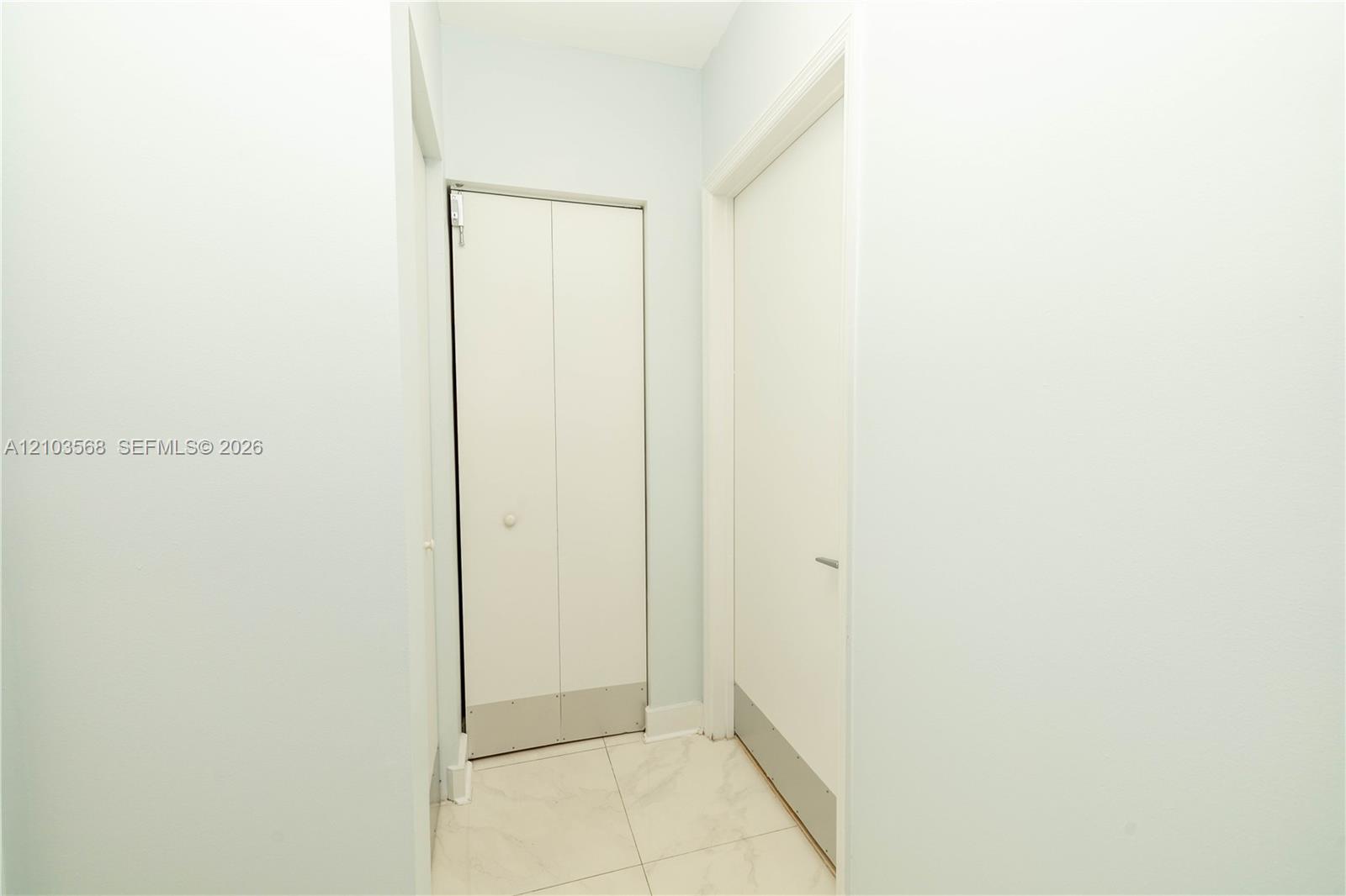 White bifold closet doors, interior door with a minimalist handle, and light-toned tile flooring