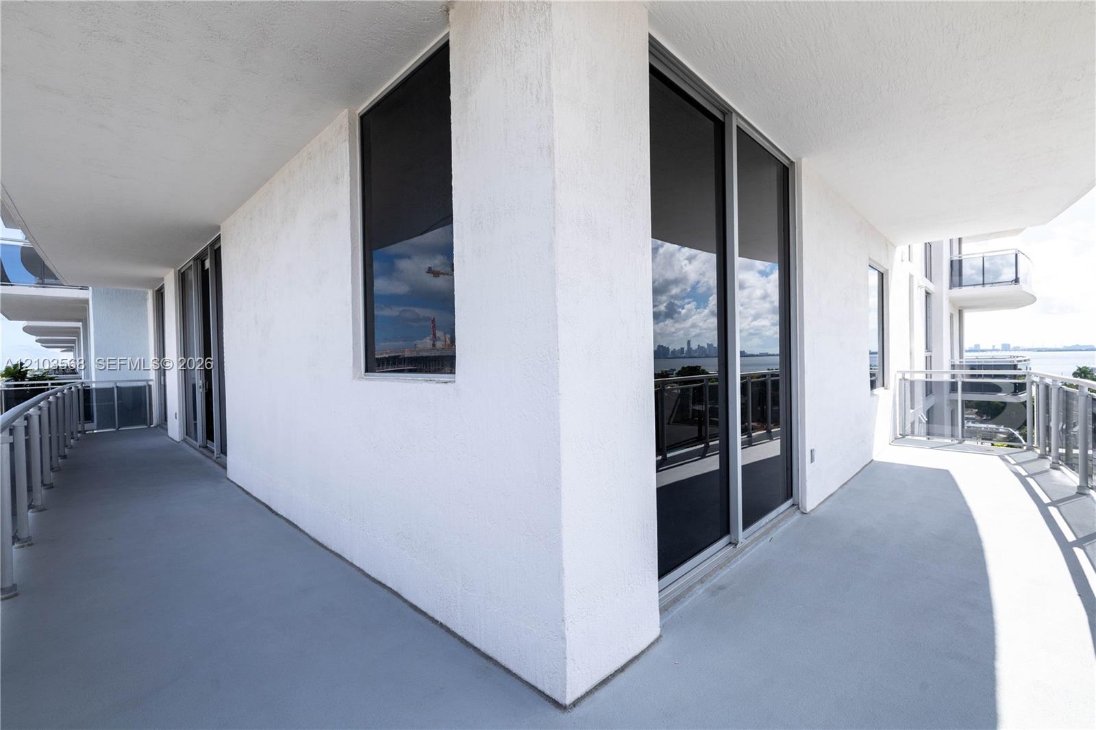 Wrap-around balcony featuring smooth concrete flooring, stucco exterior walls, metal railings, and floor-to-ceiling sliding glass doors