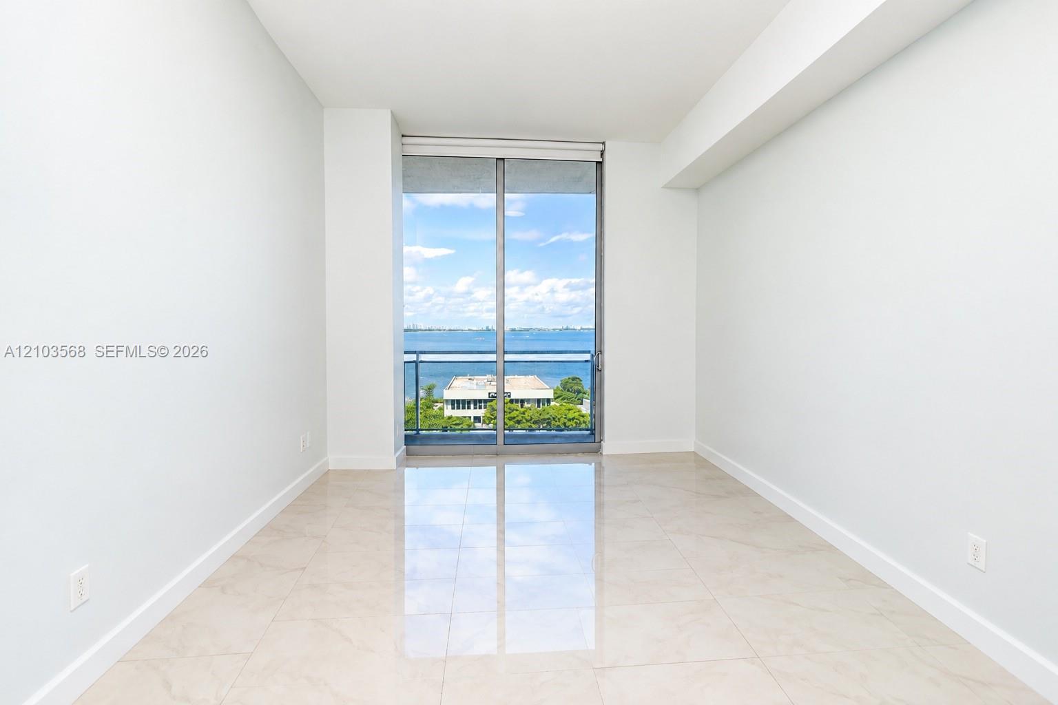 Neutral-toned tile flooring, floor-to-ceiling glass sliding door, and balcony access with water surroundings