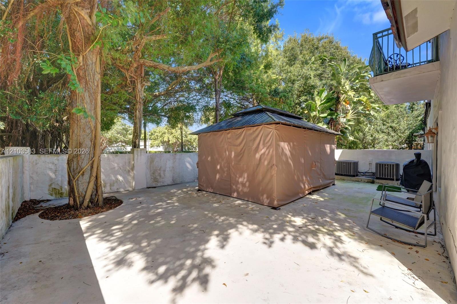 Enclosed concrete patio featuring high perimeter walls, mature trees, and a metal-roof structure