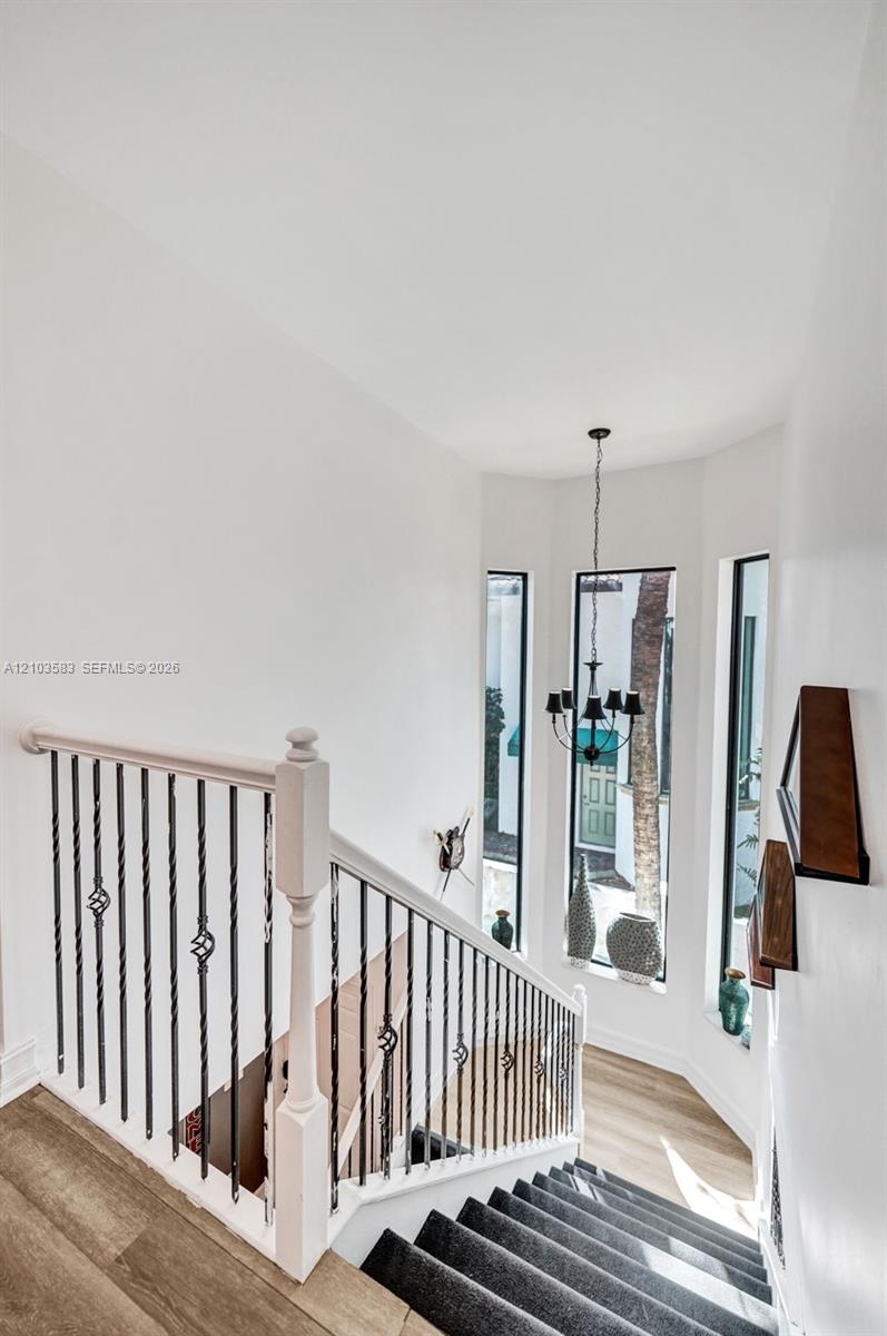 Staircase featuring a white handrail, wrought iron balusters with scroll detailing, wood-finish flooring, floor-to-ceiling windows, and a multi-arm chandelier