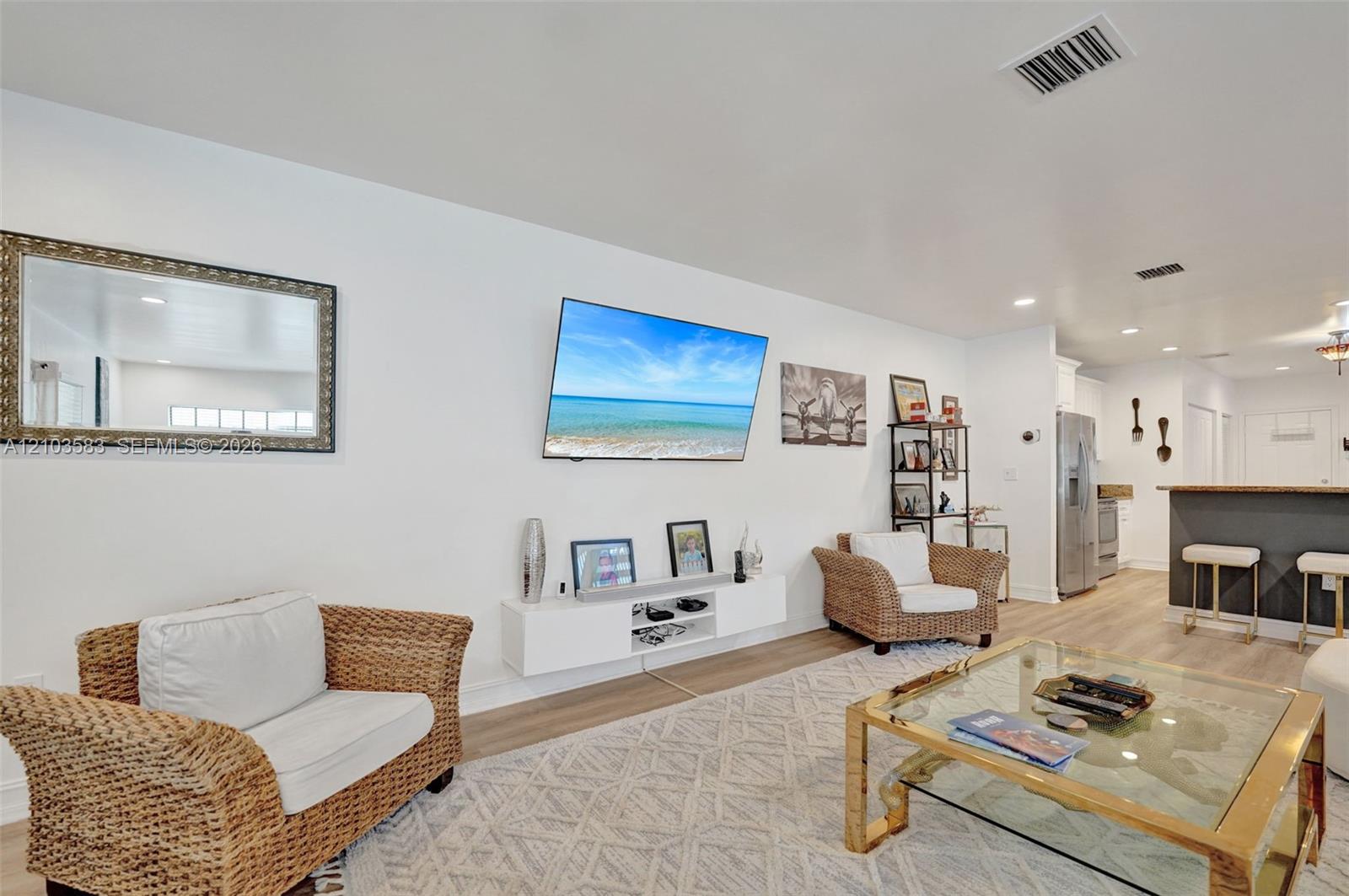 Open-concept interior featuring light-toned wood-finish flooring, recessed lighting, and a white floating media console