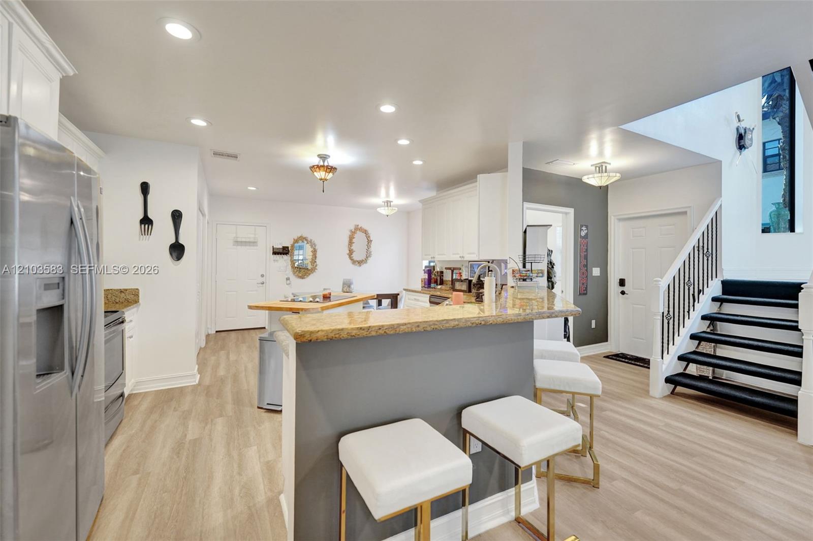 Kitchen featuring stone-surfaced breakfast bar, white cabinetry, stainless steel refrigerator, recessed lighting, and wood-finish flooring