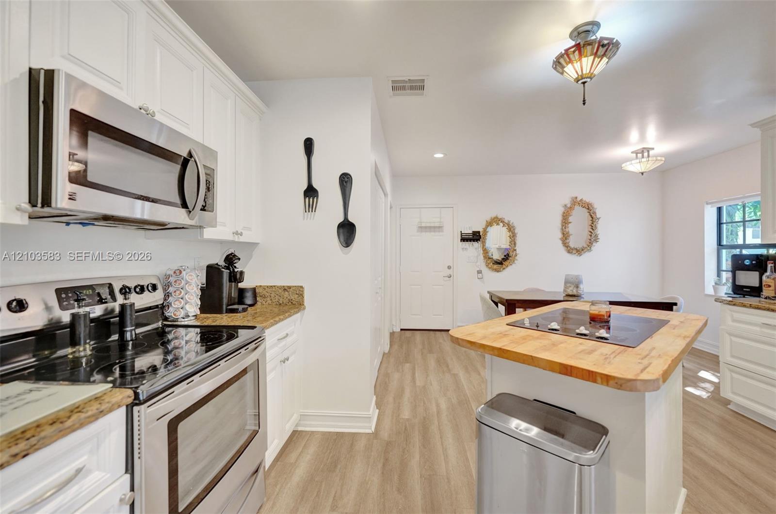 Kitchen featuring white cabinetry, stone-surface countertops, stainless steel microwave and range, wood-finish flooring, and a center island with a wood-block surface