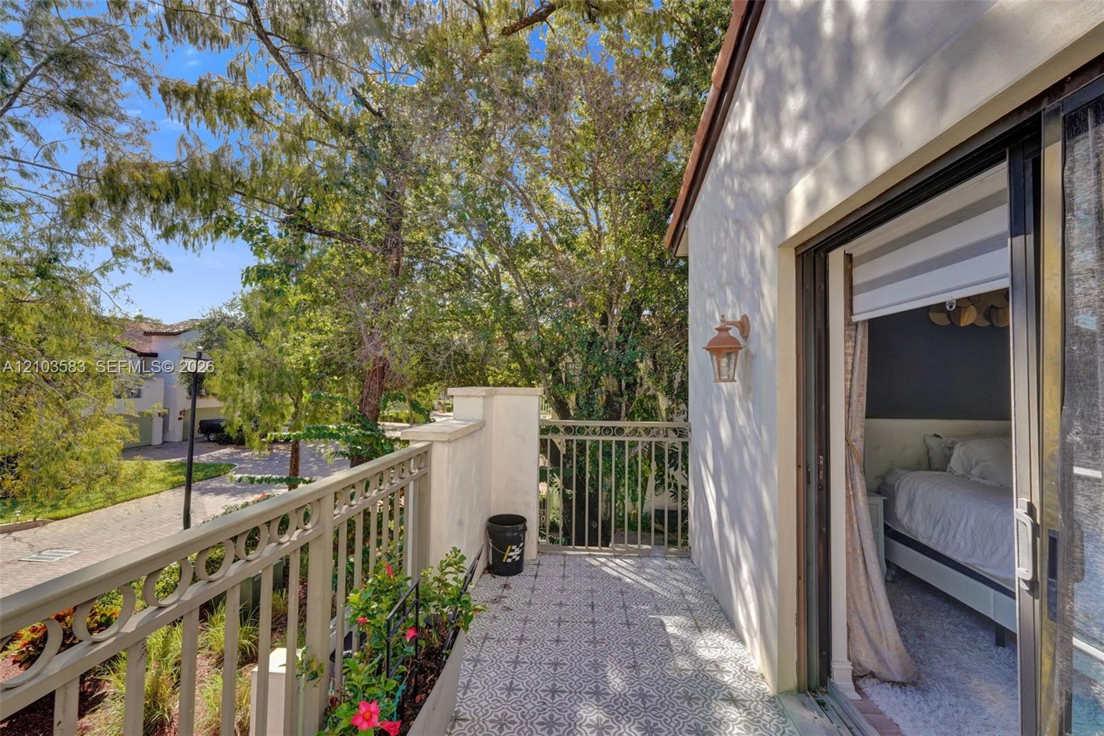 Private balcony featuring decorative tile flooring, ornate metal railing, exterior wall-mounted lighting, and sliding glass door entry