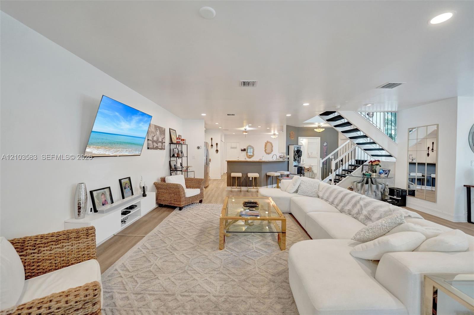 Open-concept interior featuring wood-finish flooring, recessed lighting, a built-in white media console, and a staircase with a metal railing