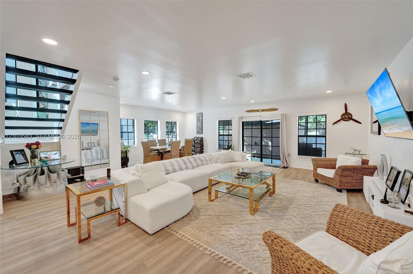 Open-concept interior featuring light-toned wood-finish flooring, recessed lighting, and a modern staircase with horizontal metal railing