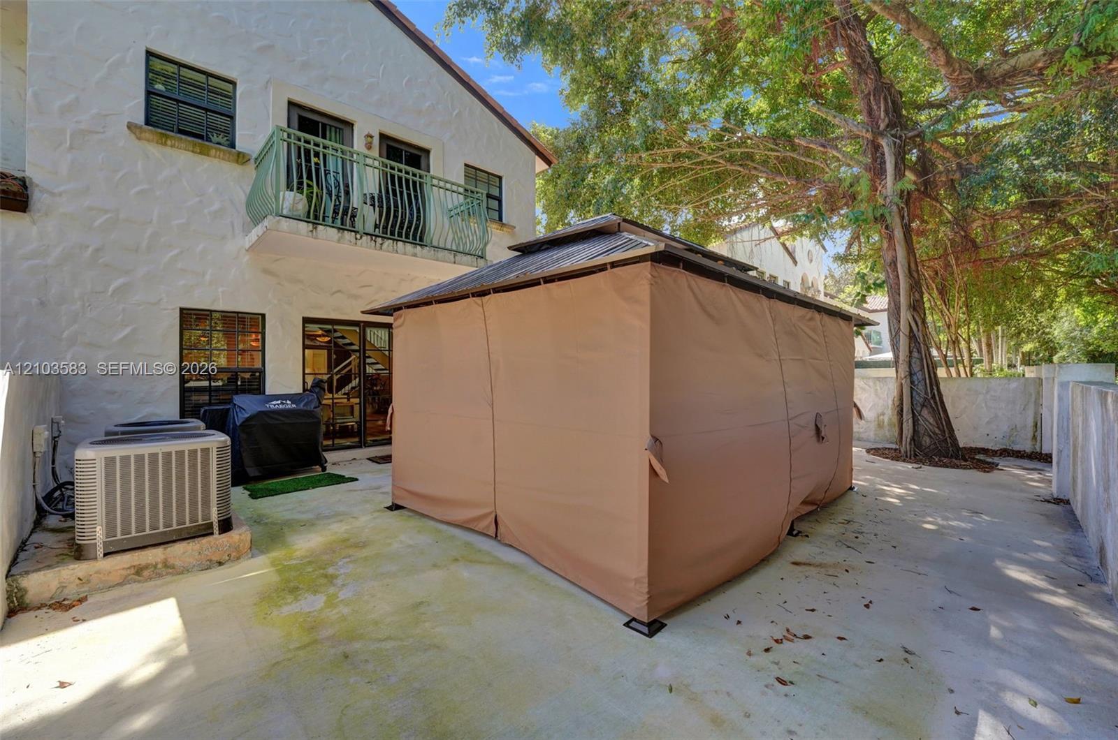 Stucco exterior featuring a second-story balcony with metal railing, concrete patio, and mature trees
