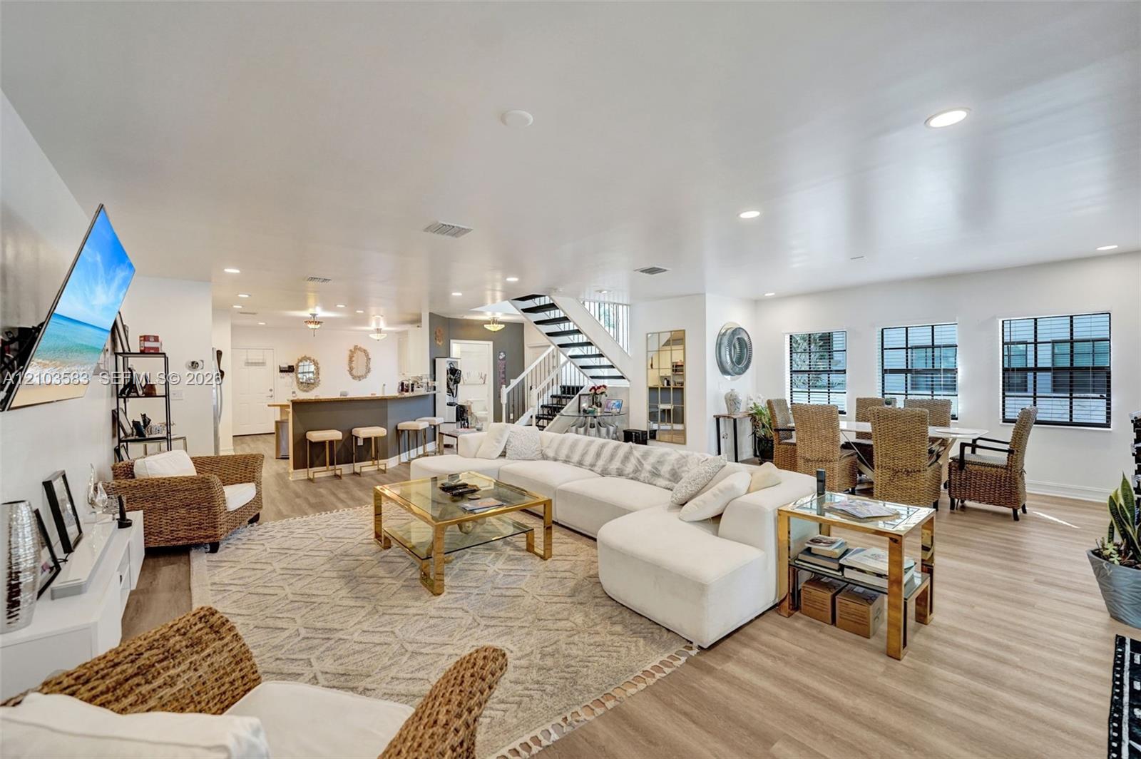 Open-concept interior featuring wood-finish flooring, recessed lighting, a breakfast bar, and a staircase with a black metal railing