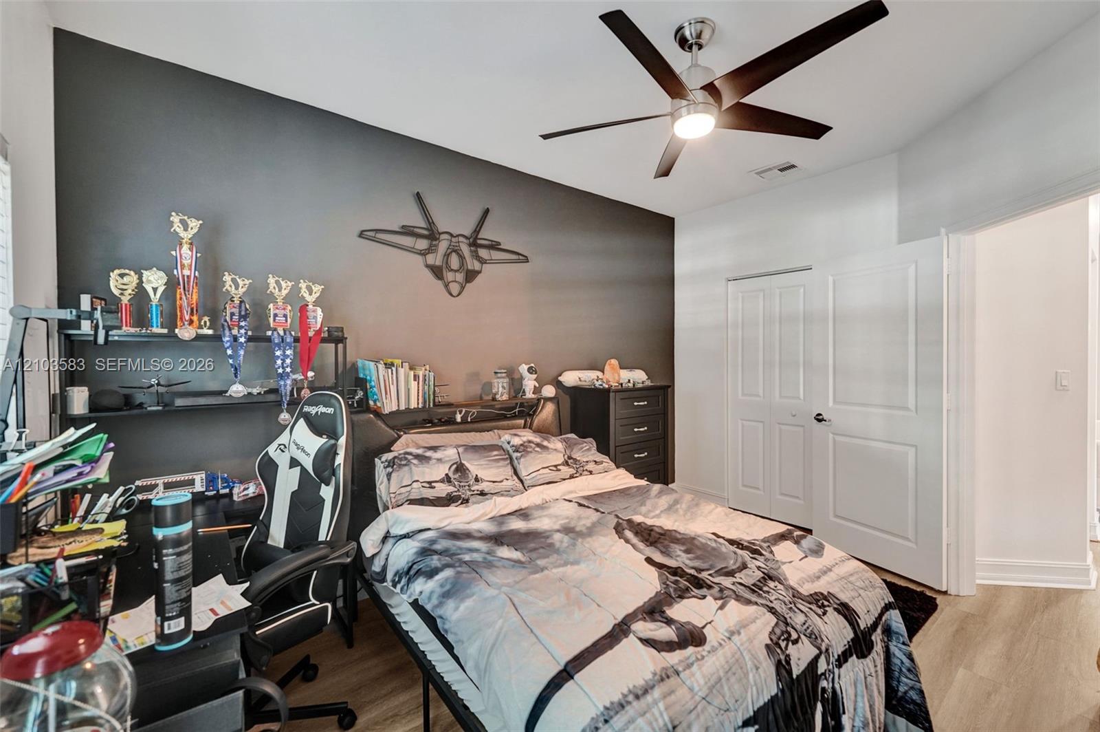 Room featuring a dark-toned accent wall, wood-finish flooring, and a modern ceiling fan with integrated lighting