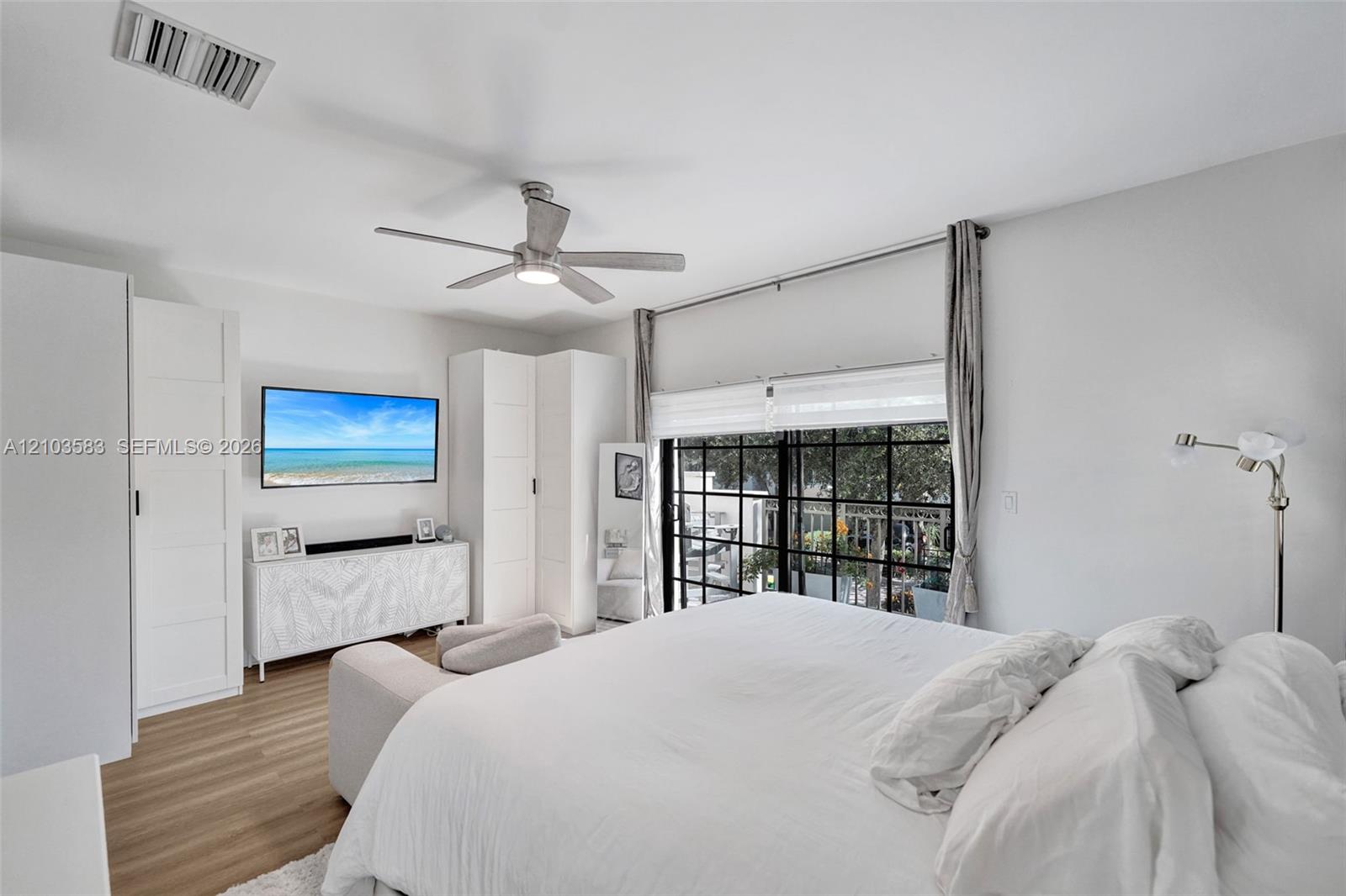 Bedroom featuring wood-finish flooring, built-in floor-to-ceiling cabinetry, a modern brushed-nickel ceiling fan, and black-framed glass sliding doors