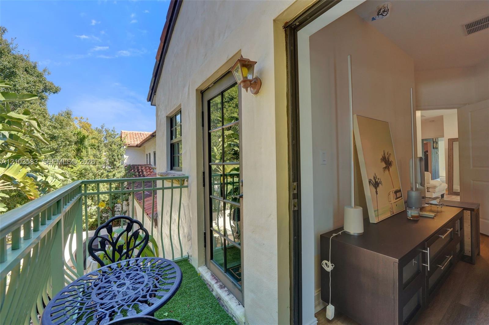 Balcony featuring sage green metal railings, exterior wall-mounted lighting, and a glass-paneled door