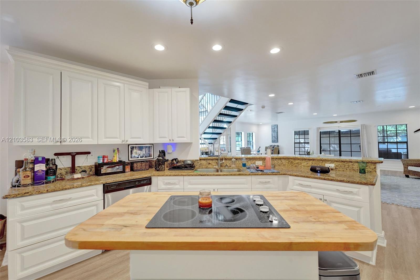 Kitchen featuring white cabinetry, stone countertops, central island with a wood-finish surface, integrated electric cooktop, and recessed lighting