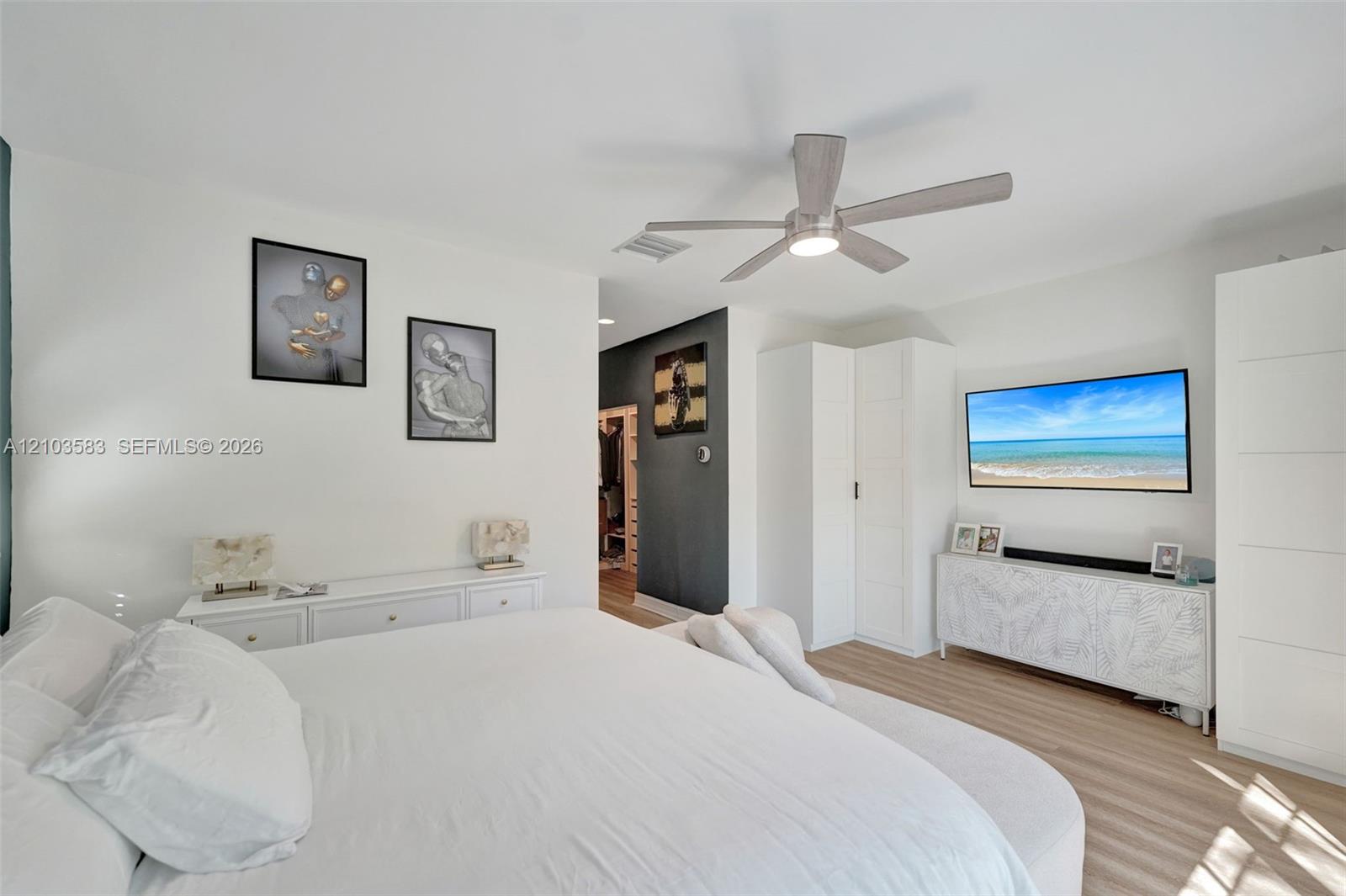 Room featuring wood-finish flooring, a neutral color palette, integrated ceiling fan with light, and built-in vertical storage cabinetry