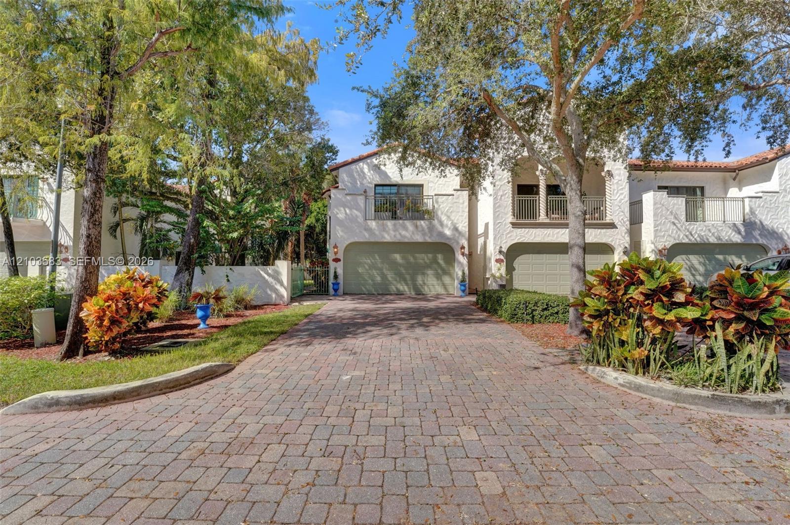 Exterior facade featuring stucco siding, multi-car garage space, second-story balconies with iron railings, paved driveway, and mature landscaping