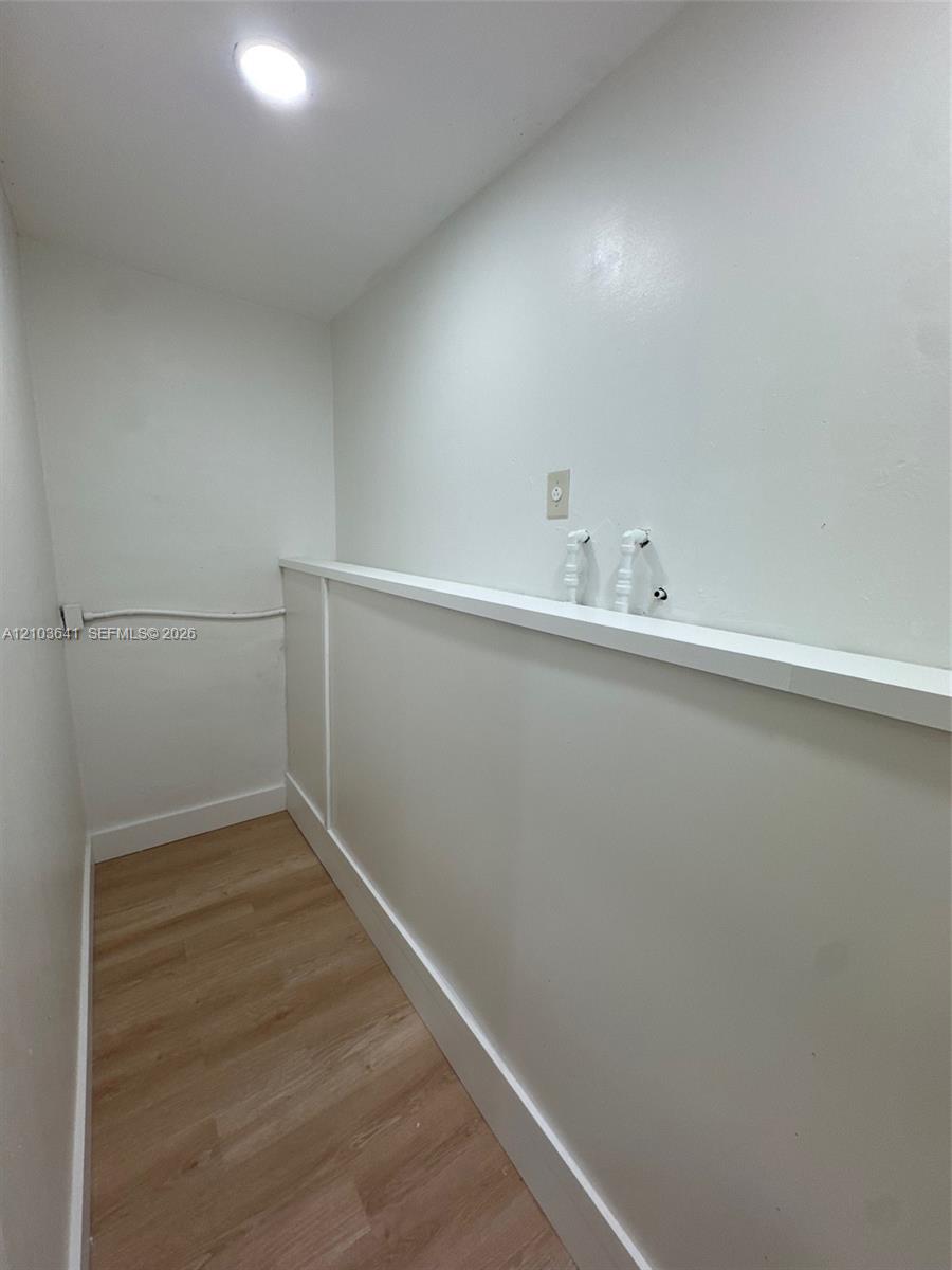 Utility area featuring wood-finish flooring, recessed ceiling lighting, and built-in plumbing connections with a mounted ledge
