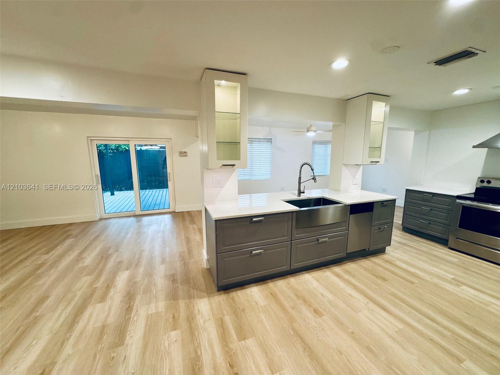 Kitchen featuring gray cabinetry, stone-finish countertops, stainless steel farmhouse sink, glass-front upper cabinets, and wood-finish flooring