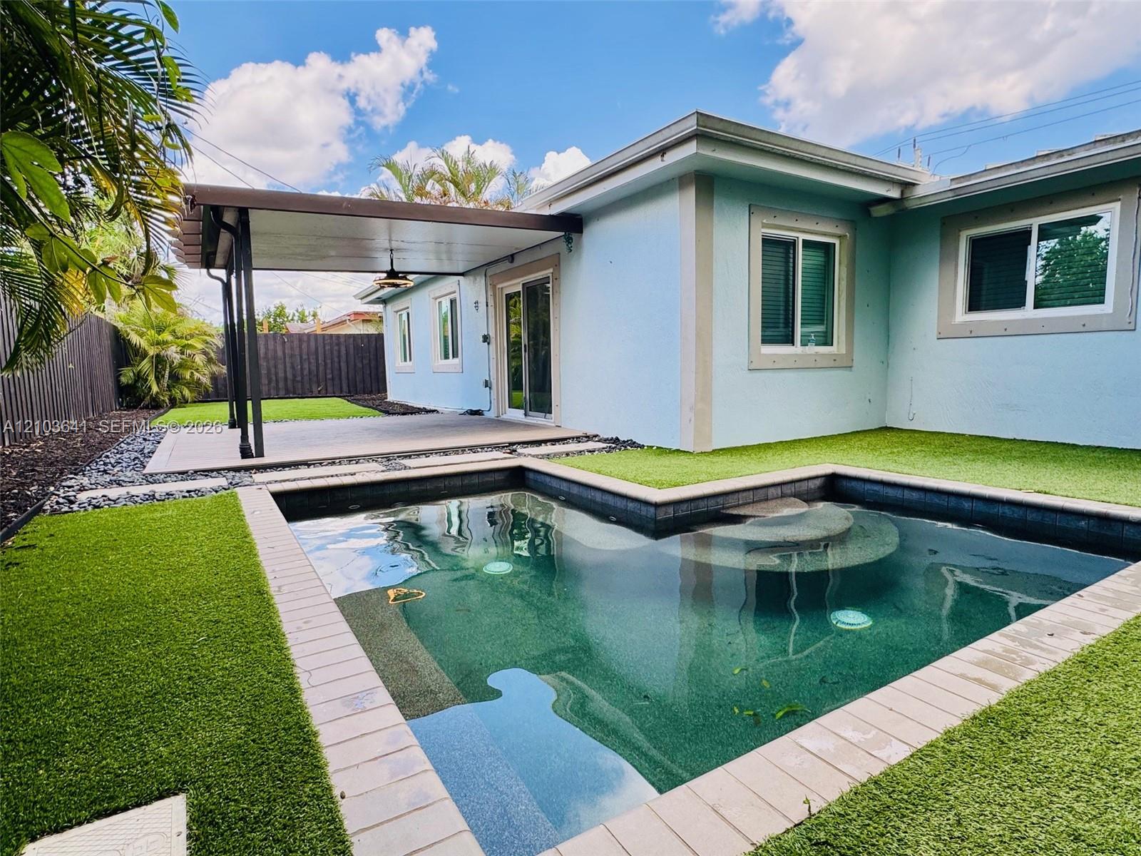 Outdoor space featuring an in-ground pool with stone coping, synthetic turf, a covered patio with a ceiling fan, and privacy fencing