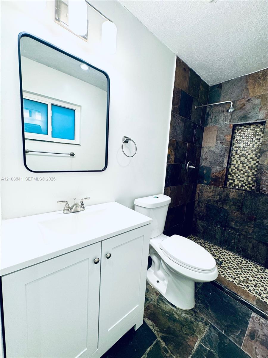 White vanity with integrated sink, rectangular mirror with black frame, multi-tone slate tile shower surround, mosaic tile shower inlay, and stone-finish floor tiling