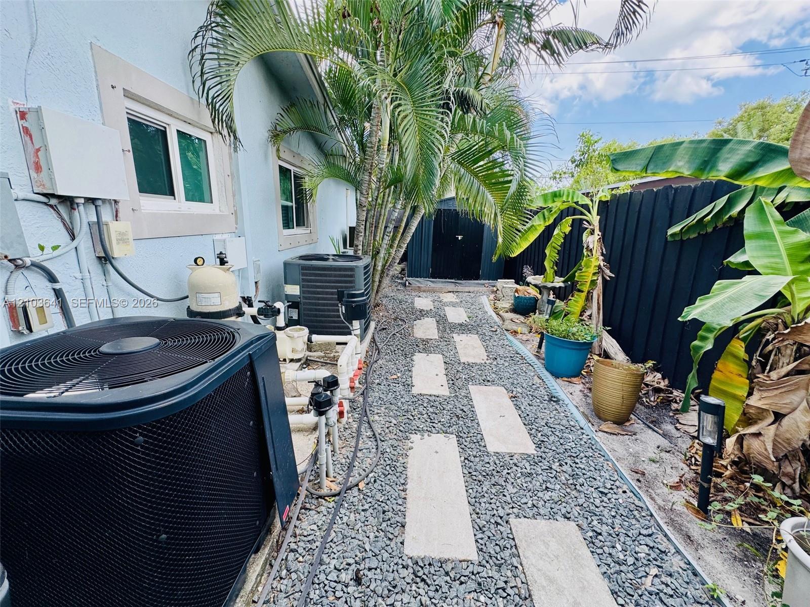 Side yard featuring a stone-paver walkway, dark privacy fencing, and exterior mechanical equipment
