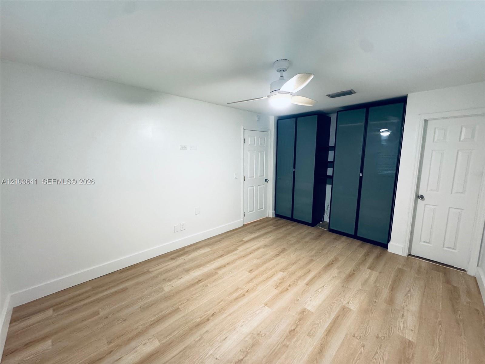 Wood-finish flooring, white walls, built-in cabinetry with frosted glass panels, and a ceiling-mounted light fixture with fan