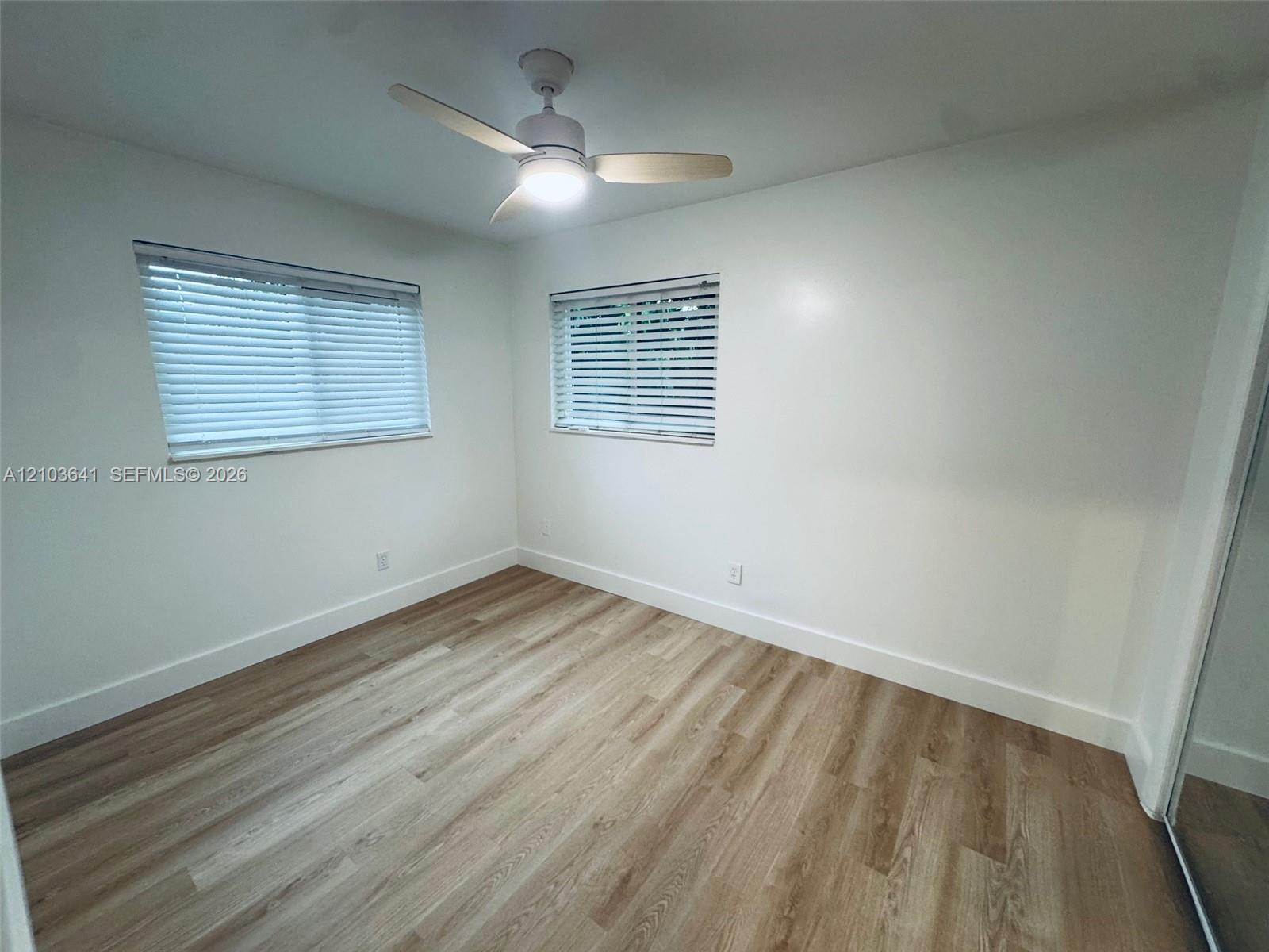 Room featuring wood-finish flooring, dual windows with horizontal blinds, and a white ceiling fan with integrated lighting