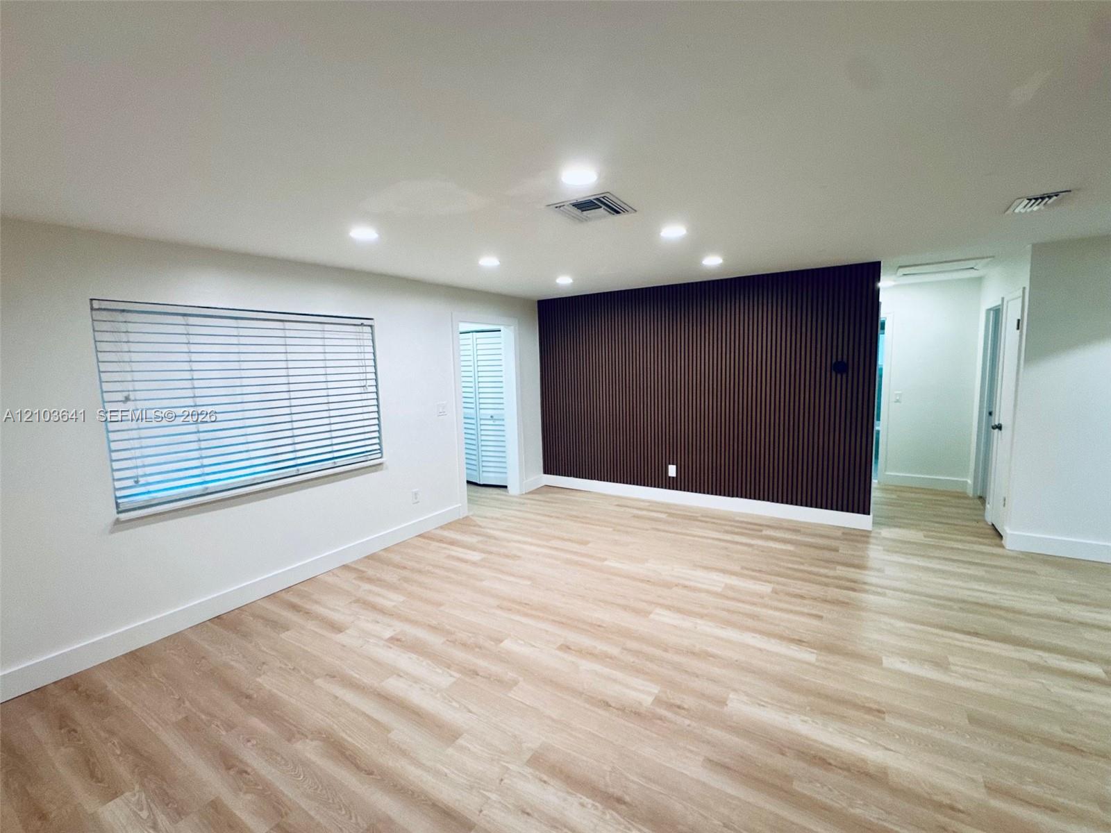 Wood-finish flooring, dark fluted accent wall, recessed lighting, and horizontal blind window treatments