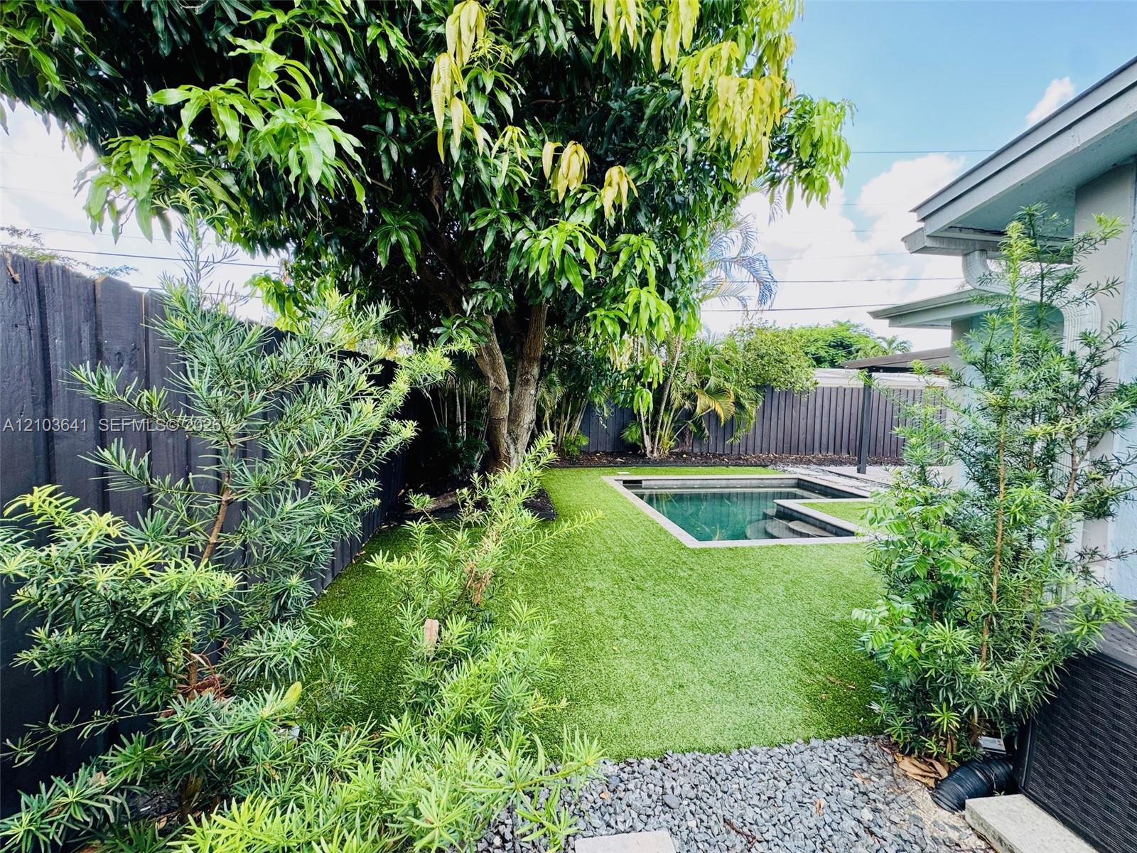 Backyard area featuring a rectangular pool, synthetic turf lawn, stone gravel perimeter, and a dark-toned privacy fence