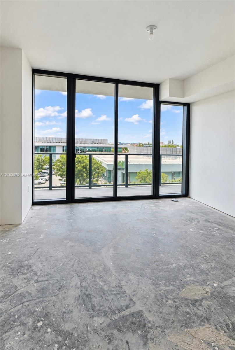 Floor-to-ceiling windows with black frames, concrete flooring, and access to an exterior balcony