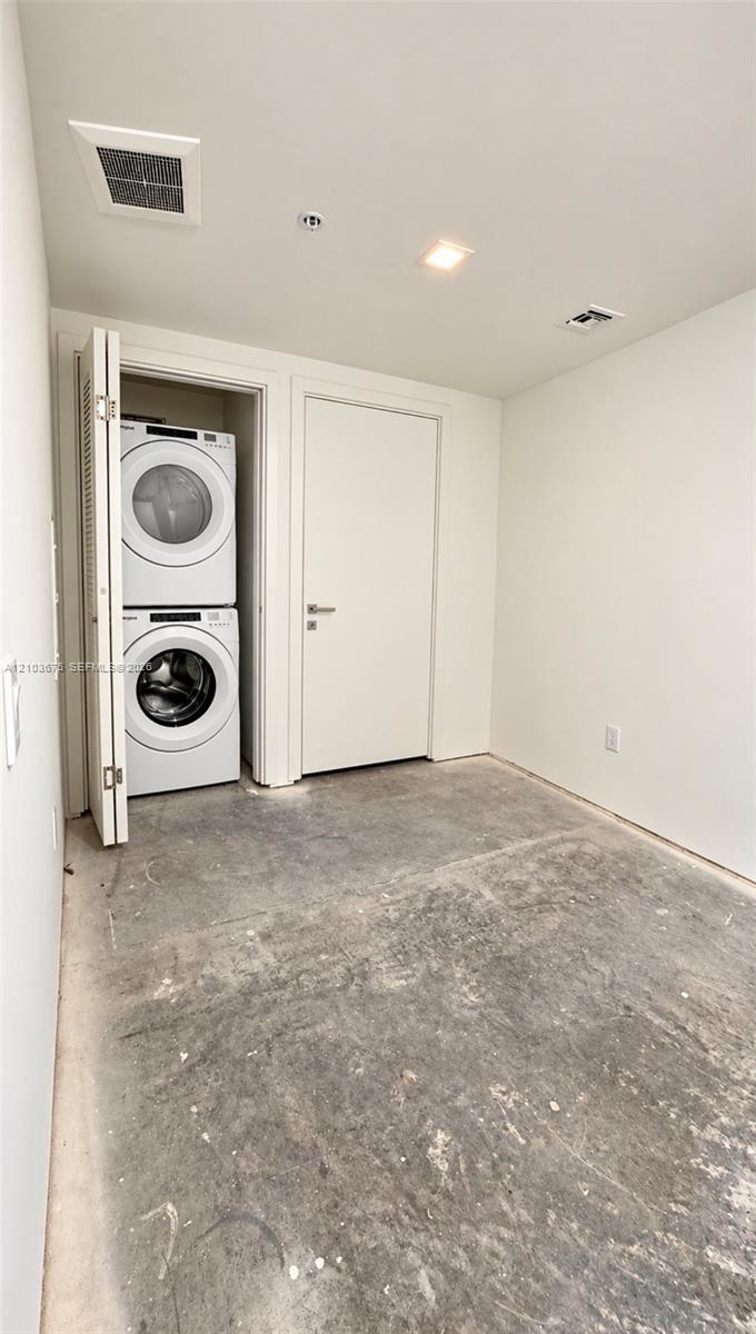 Stacked laundry unit with white appliances, enclosed within a closet featuring bi-fold doors, complemented by recessed ceiling lighting and a flat-panel interior door