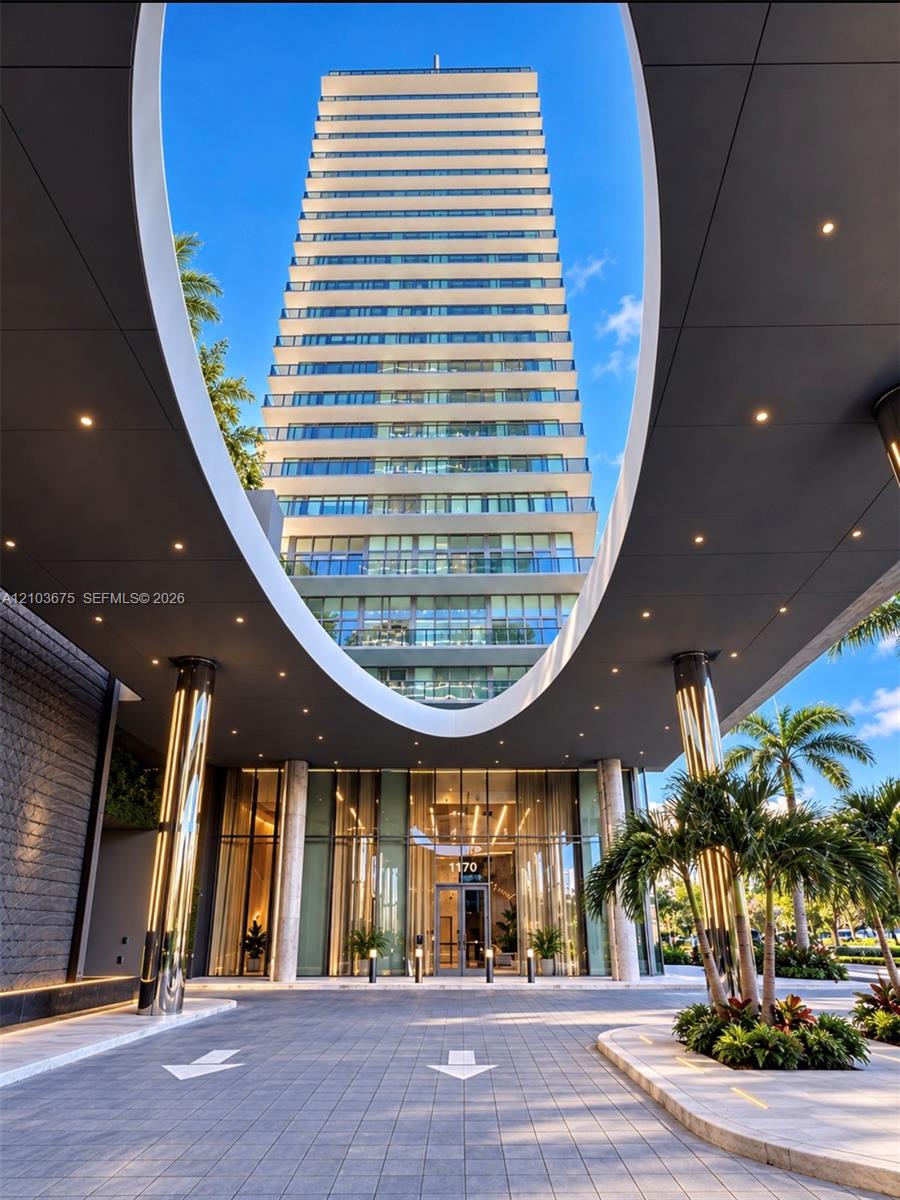 High-rise exterior featuring a circular porte-cochre, recessed lighting, glass-paneled balconies, floor-to-ceiling glass entrance, and a paved motor court
