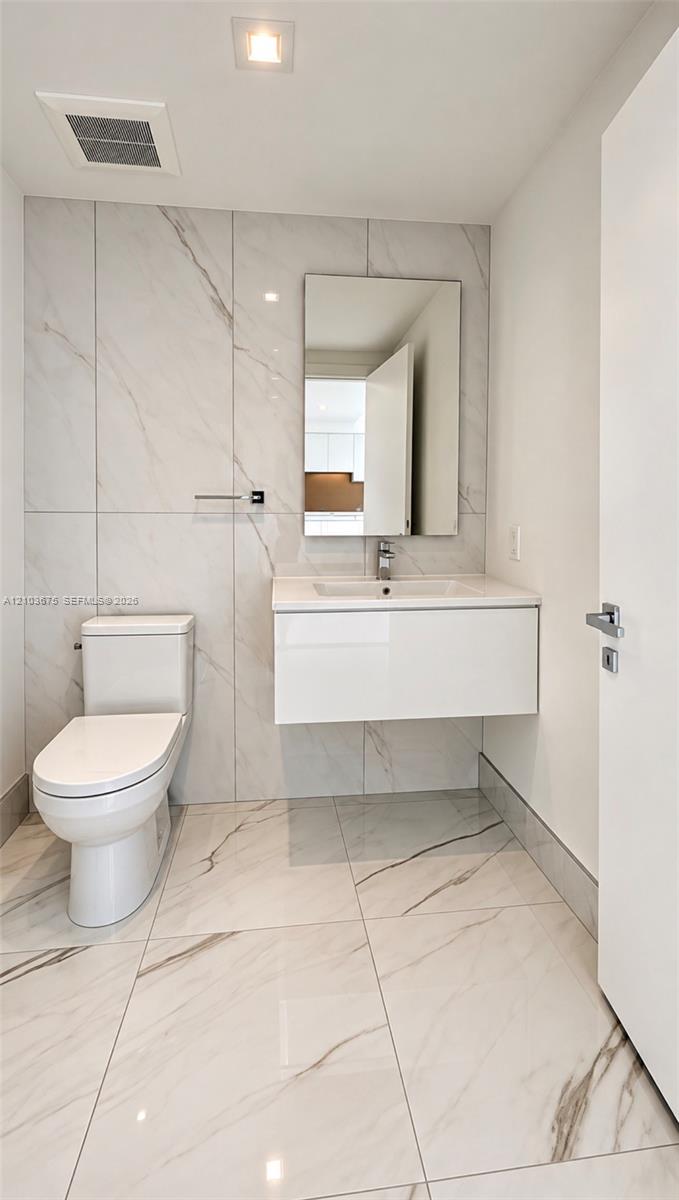 Floating vanity with a white integrated basin, floor-to-ceiling large-format tile wall, white stone-patterned floor tiling, rectangular mirror, and chrome single-handle faucet