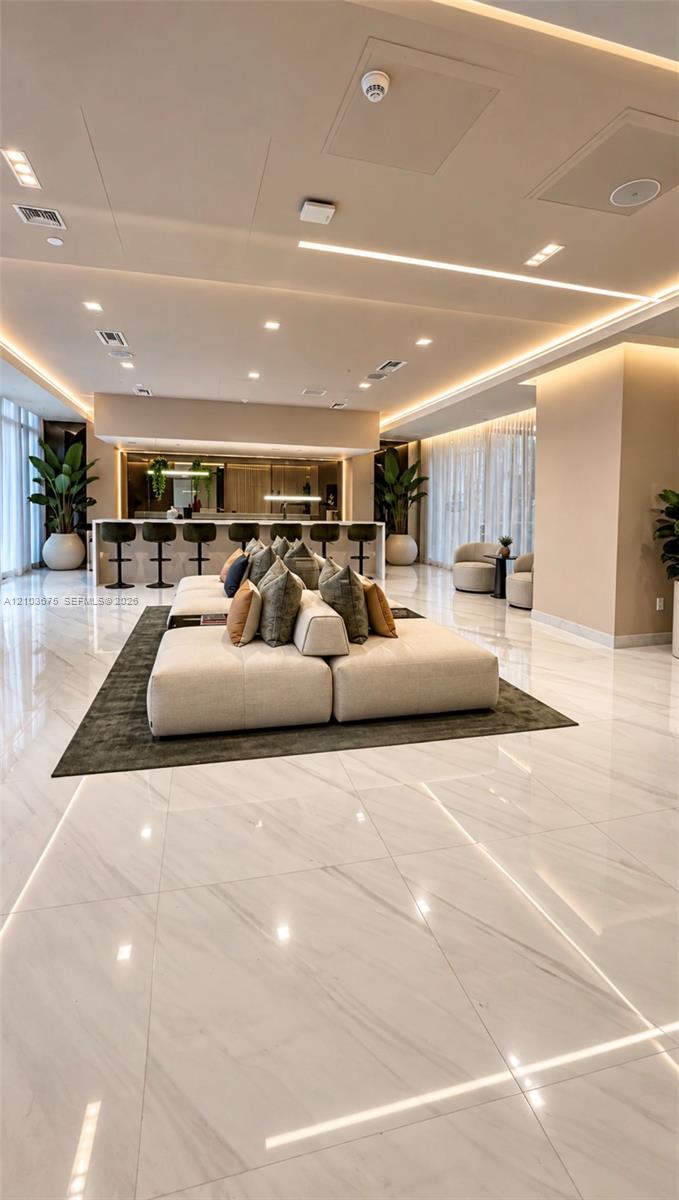 Polished stone-finish flooring throughout, tray ceiling with integrated recessed and linear LED lighting, and a built-in bar area featuring a stone countertop