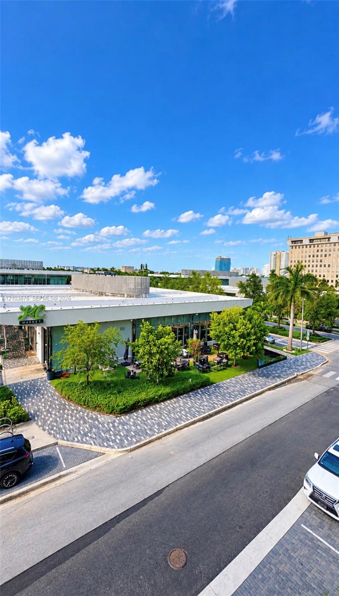 Commercial property featuring a flat roofline, floor-to-ceiling glass paneling, patterned paver walkways, and established green space with mature landscaping