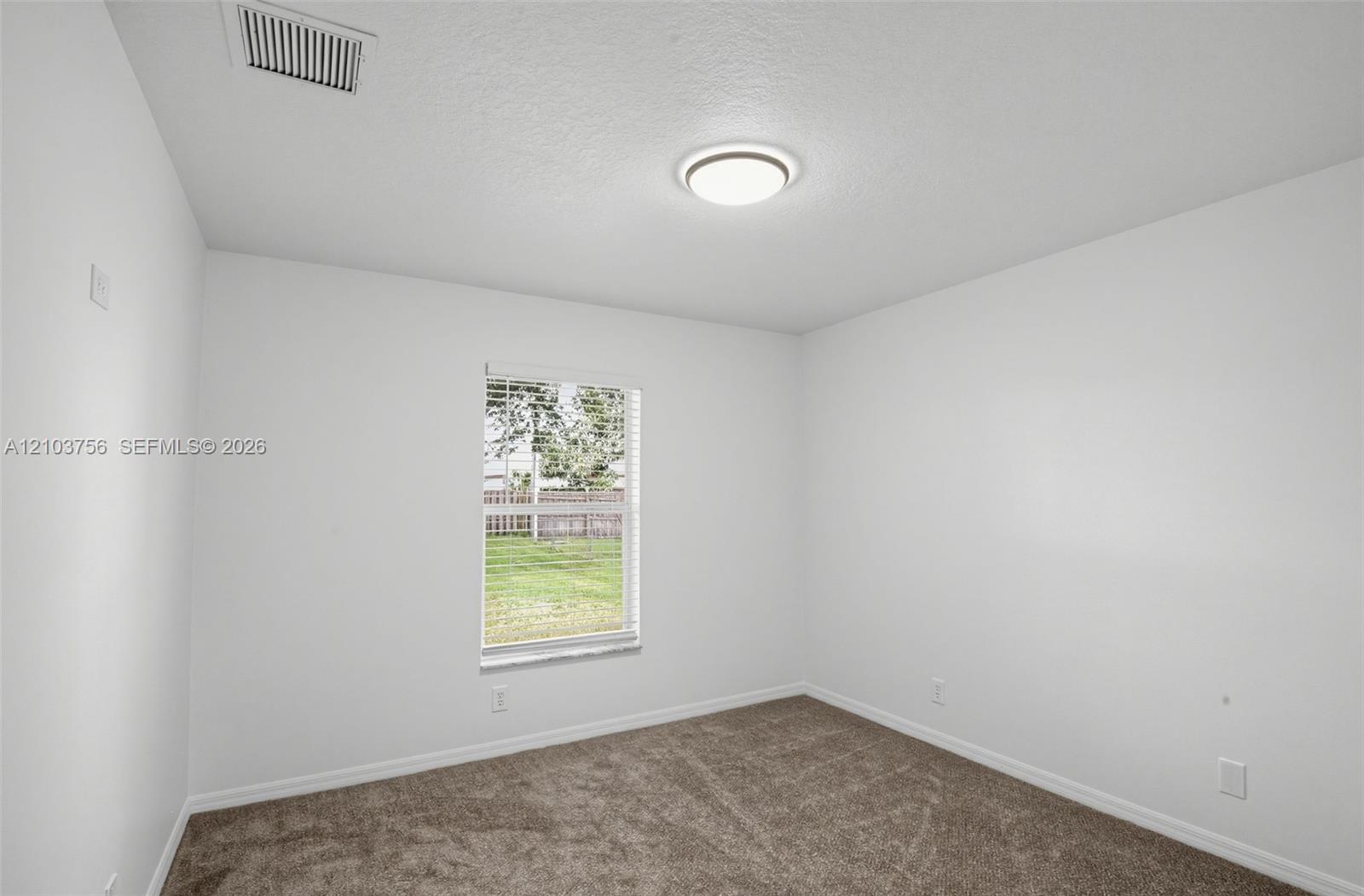 Neutral-toned carpeting, crisp white wall finish, flush-mount circular lighting fixture, and a single-pane window with horizontal blinds