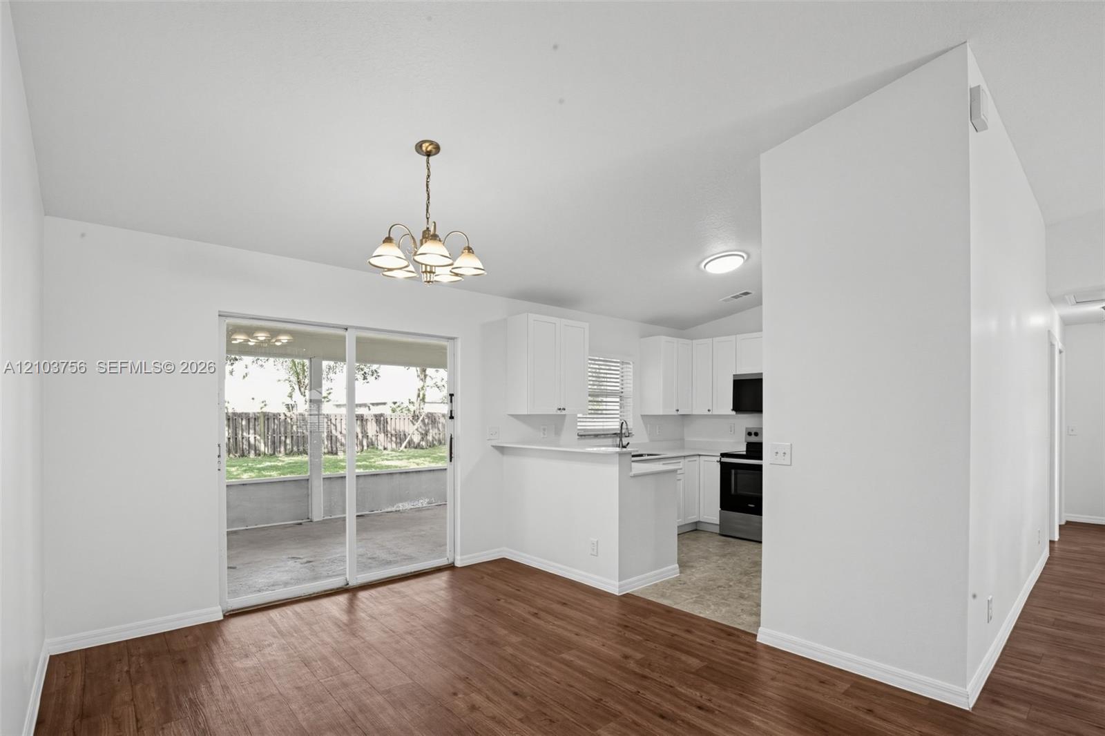 Open-concept space featuring wood-finish flooring, a multi-light chandelier, and a sliding glass door providing external access