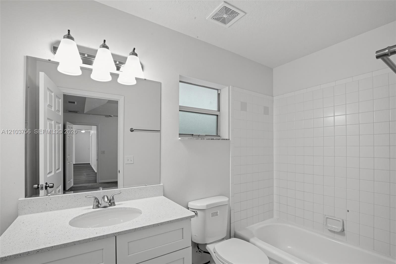 Bathroom featuring a vanity with a white countertop and oval under-mount sink, three-light fixture, wall-mounted mirror, and white tile tub surround