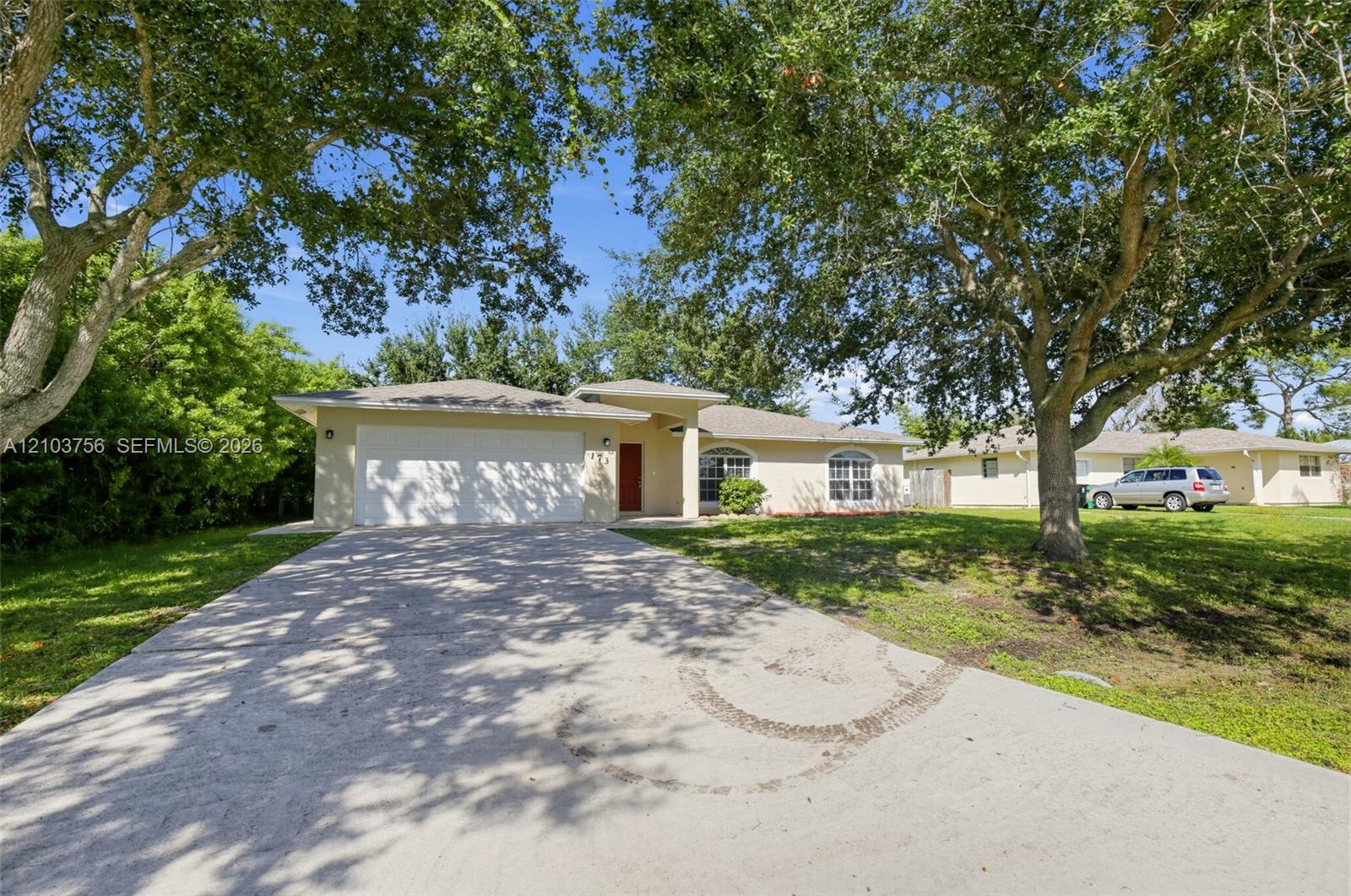 Single-story residence featuring a stucco exterior, an attached two-car garage, arched windows, and mature trees on a lot with lawn space