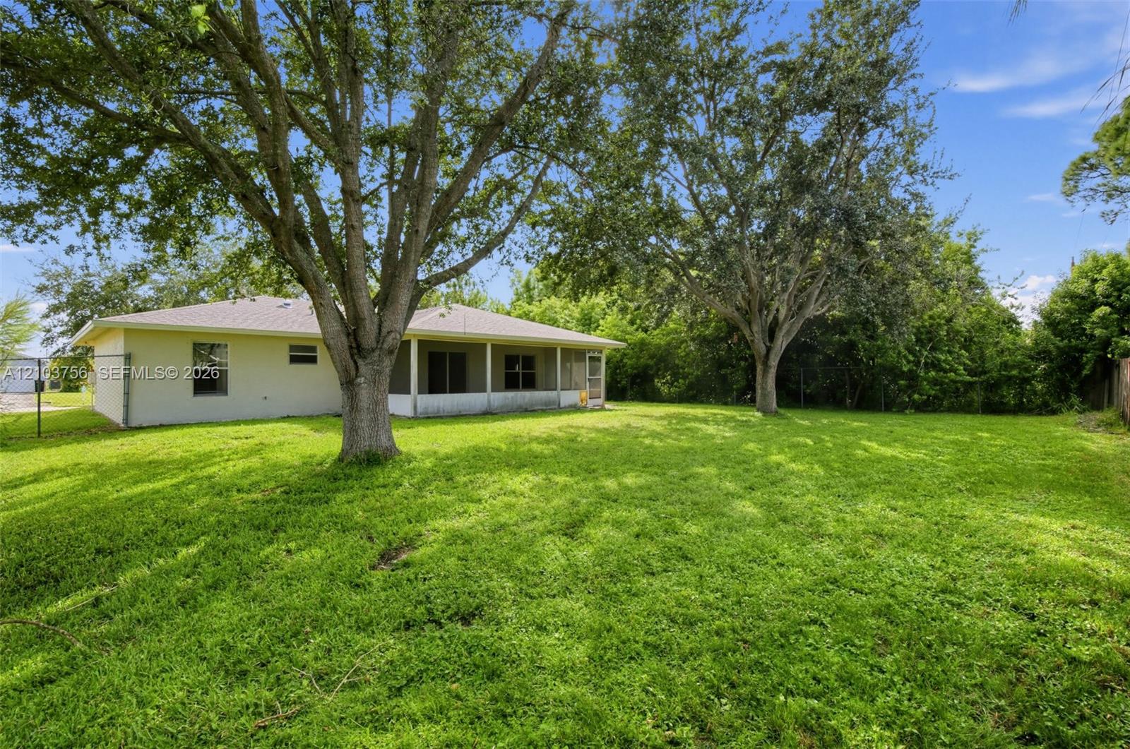 Spacious backyard featuring mature trees, a covered patio with screening, and light-colored stucco exterior siding