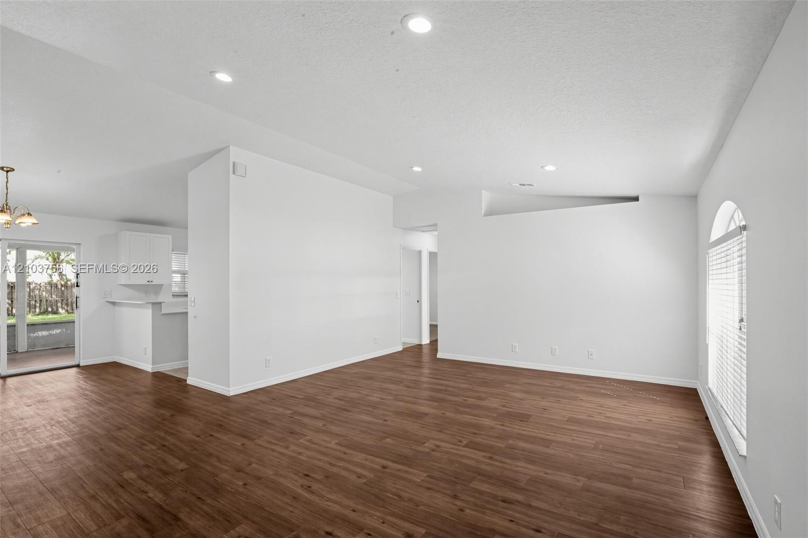 Open-concept interior featuring wood-finish flooring, recessed lighting, vaulted ceilings, and an arched window