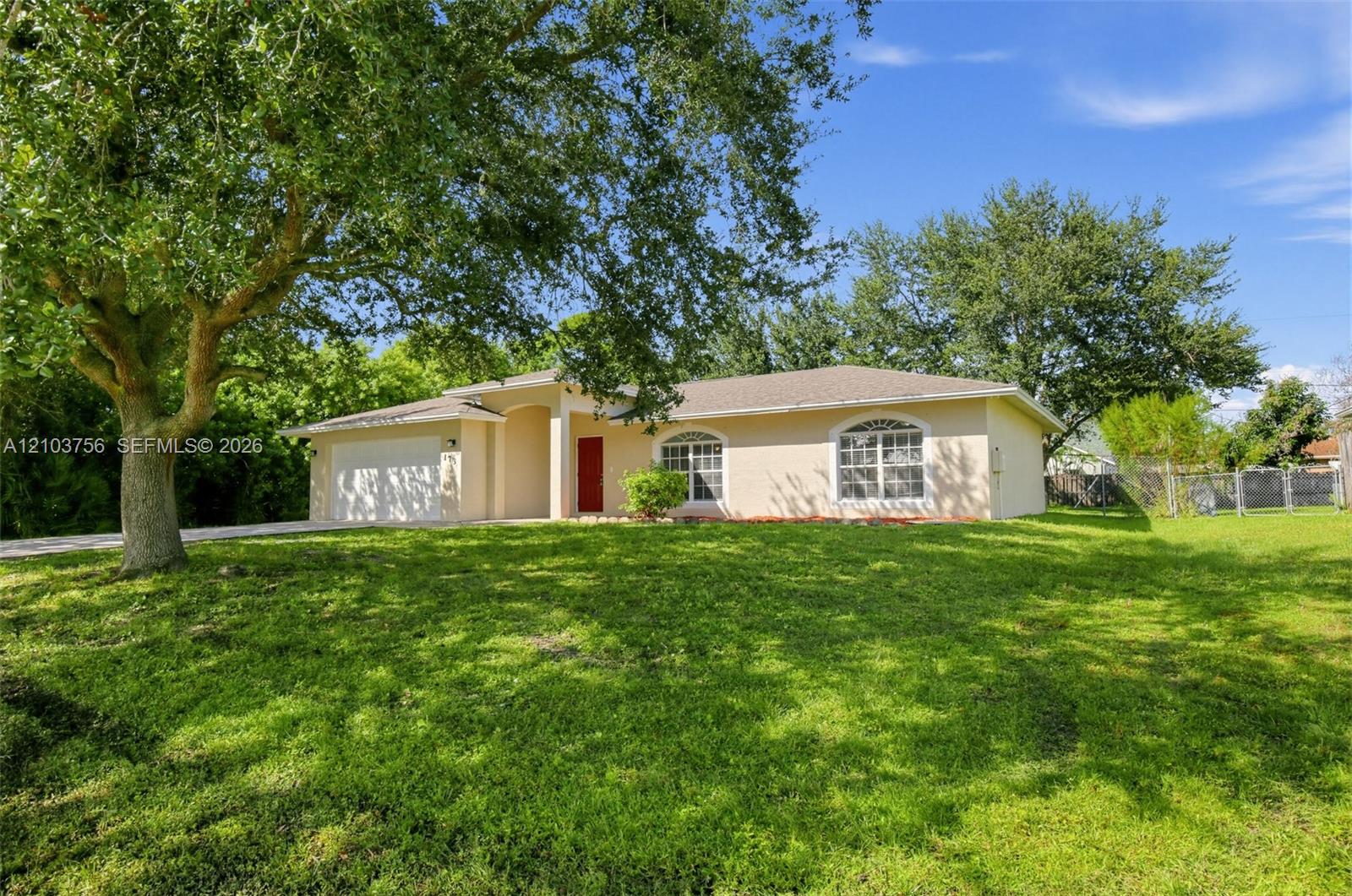 Single-story exterior featuring light-toned stucco siding, an arched entryway, arched windows with muntin detailing, a two-car garage, and mature trees situated on a grass-covered lot