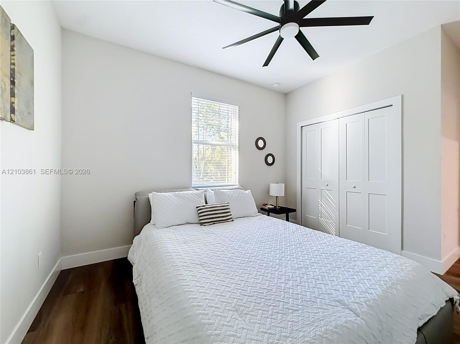Room featuring wood-finish flooring, a matte black ceiling fan, and white paneled sliding closet doors