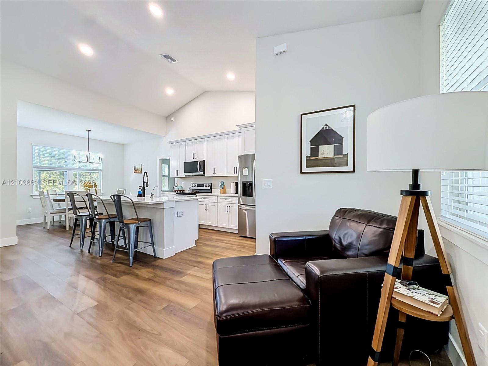 Vaulted ceilings, wood-finish flooring, white shaker-style cabinetry, kitchen island with stone-finish countertop, and recessed lighting