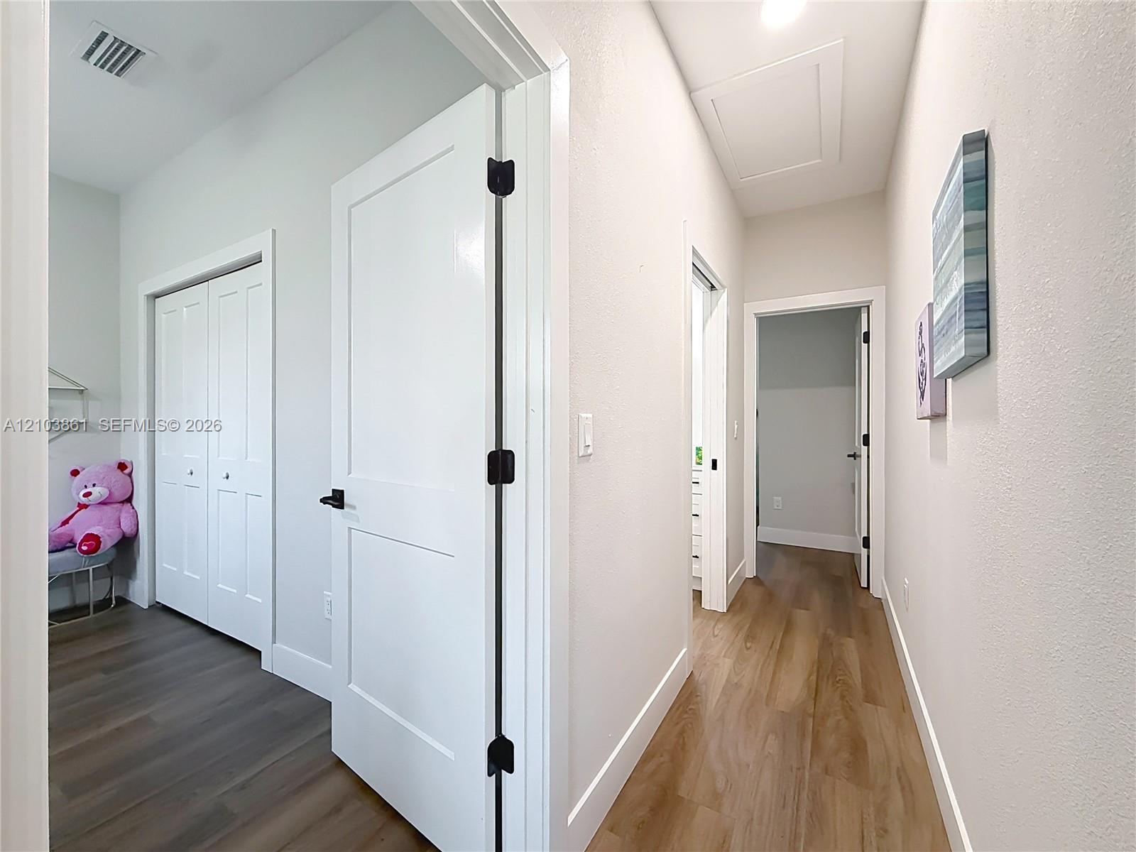 Interior hallway featuring wood-finish flooring, two-panel shaker style doors, and matte black hardware