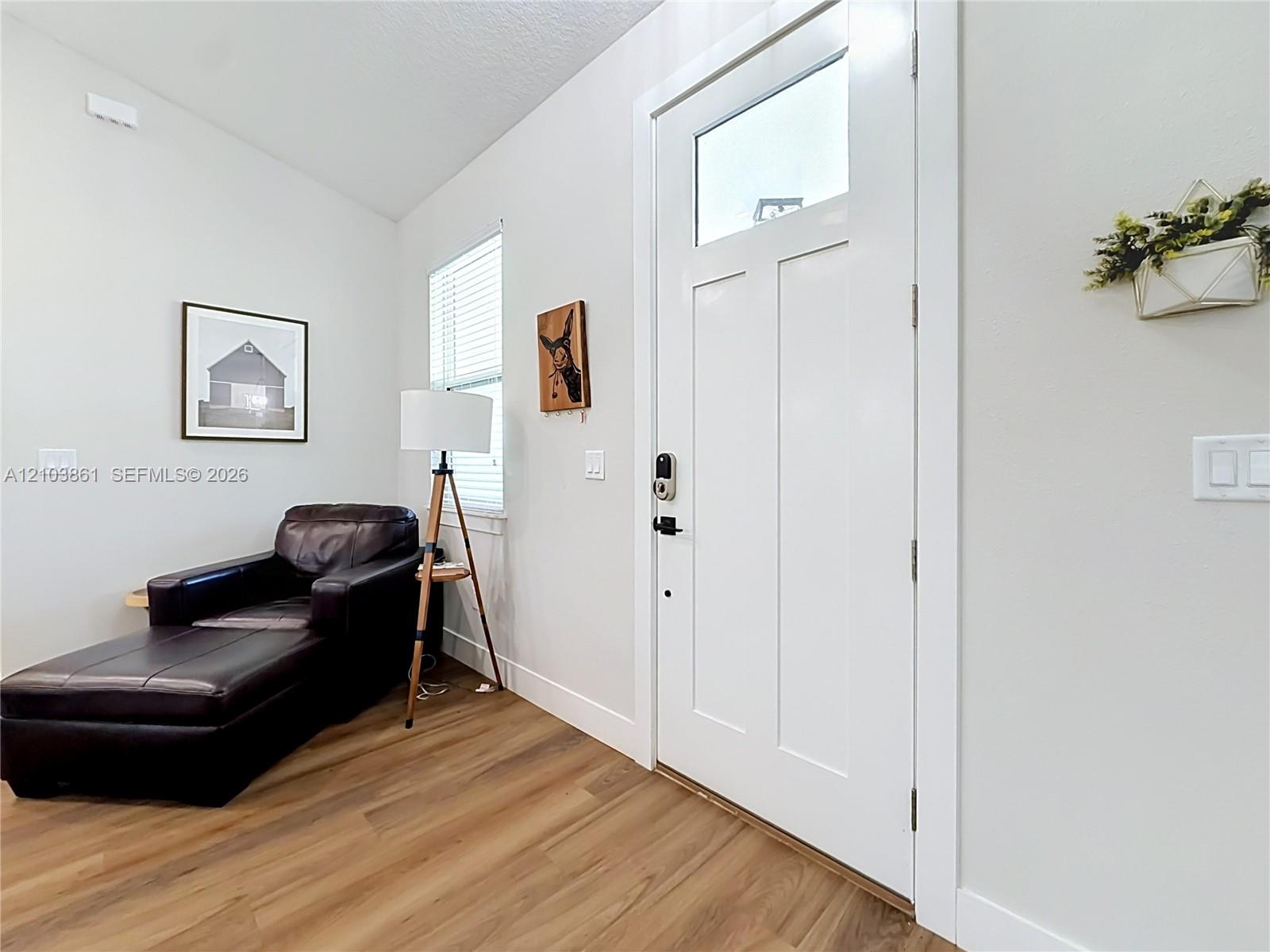 Entrance featuring a white door with an upper glass pane, neutral wall paint, wood-finish flooring, and a single-hung window with blinds